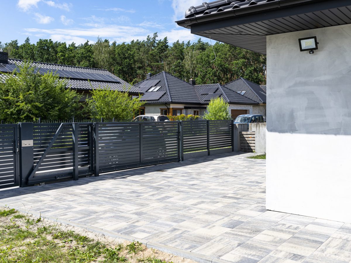 A modern panel fence in anthracite color, a visible sliding gate to the garage and a wicket with a letterbox.